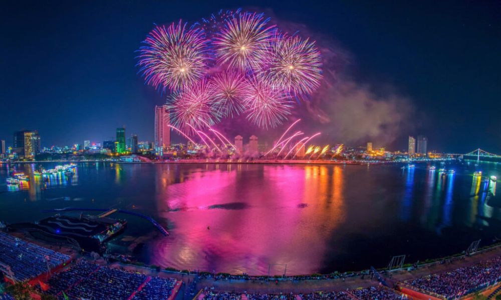 Pháo hoa màu hồng và tím ngoạn mục của lễ hội pháo hoa Đà Nẵng soi bóng xuống sông, tạo nên cảnh sắc huyền ảo